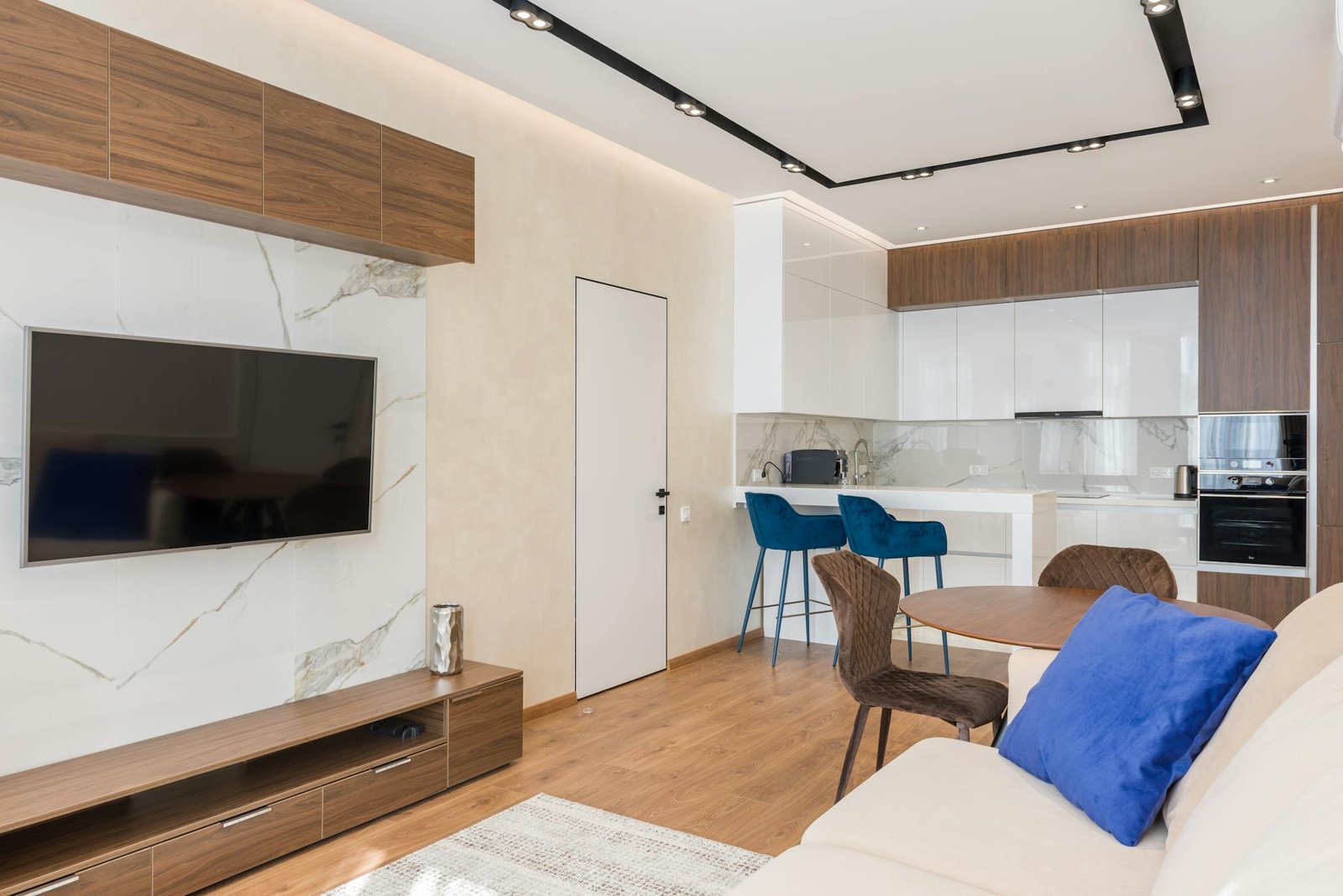 Interior of living room and open kitchen with comfortable sofa TV and chairs placed near round table in modern apartment